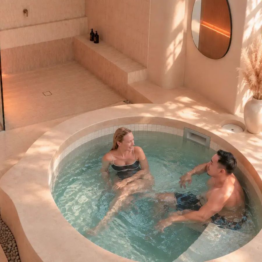 a couple relaxing in the cold plunge of a private sundaymood suite in bangkok, infrared sauna behind